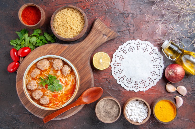 En Kolay Ekşili Köfte Çorbası Tarifi (Tam Ölçü, Ev Usulü) 2 horizontal view tomato meatballs soup with noodles brown bowl different spices oil bottle onion garlic napkin dark background 2